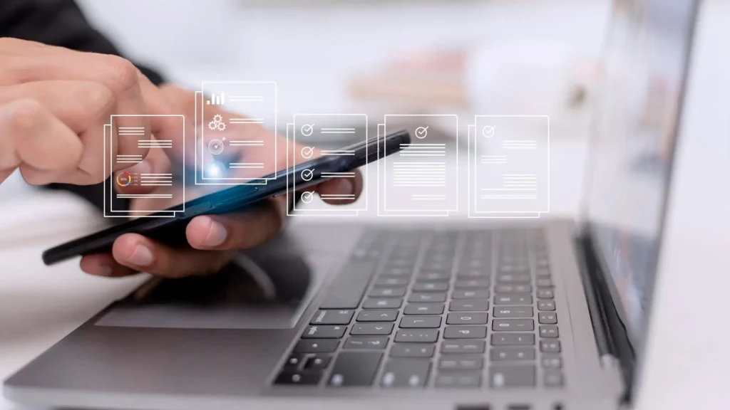 A hand holding a smartphone, with digital icons representing documents and checklists floating above a laptop keyboard, symbolizing the transaction process