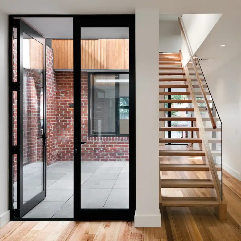 A modern home featuring a large hinged door and wooden stairs, showcasing the craftsmanship of the best Aluminum Door Manufacturer