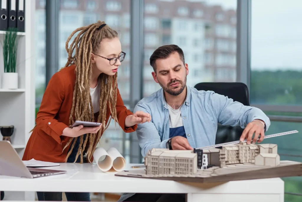 Man and woman reviewing architectural plans and a scale model of a building in an office setting