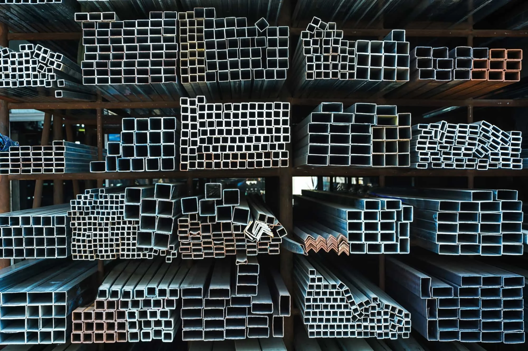 Rows of variously sized square and rectangular metal tubes neatly stacked on shelves in a warehouse