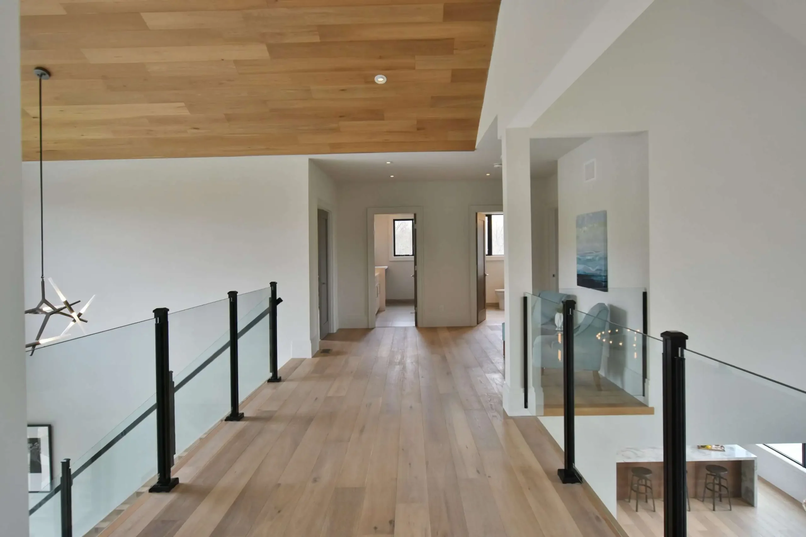 A hallway featuring elegant wooden floors complemented by modern glass railings showcasing a stylish interior design