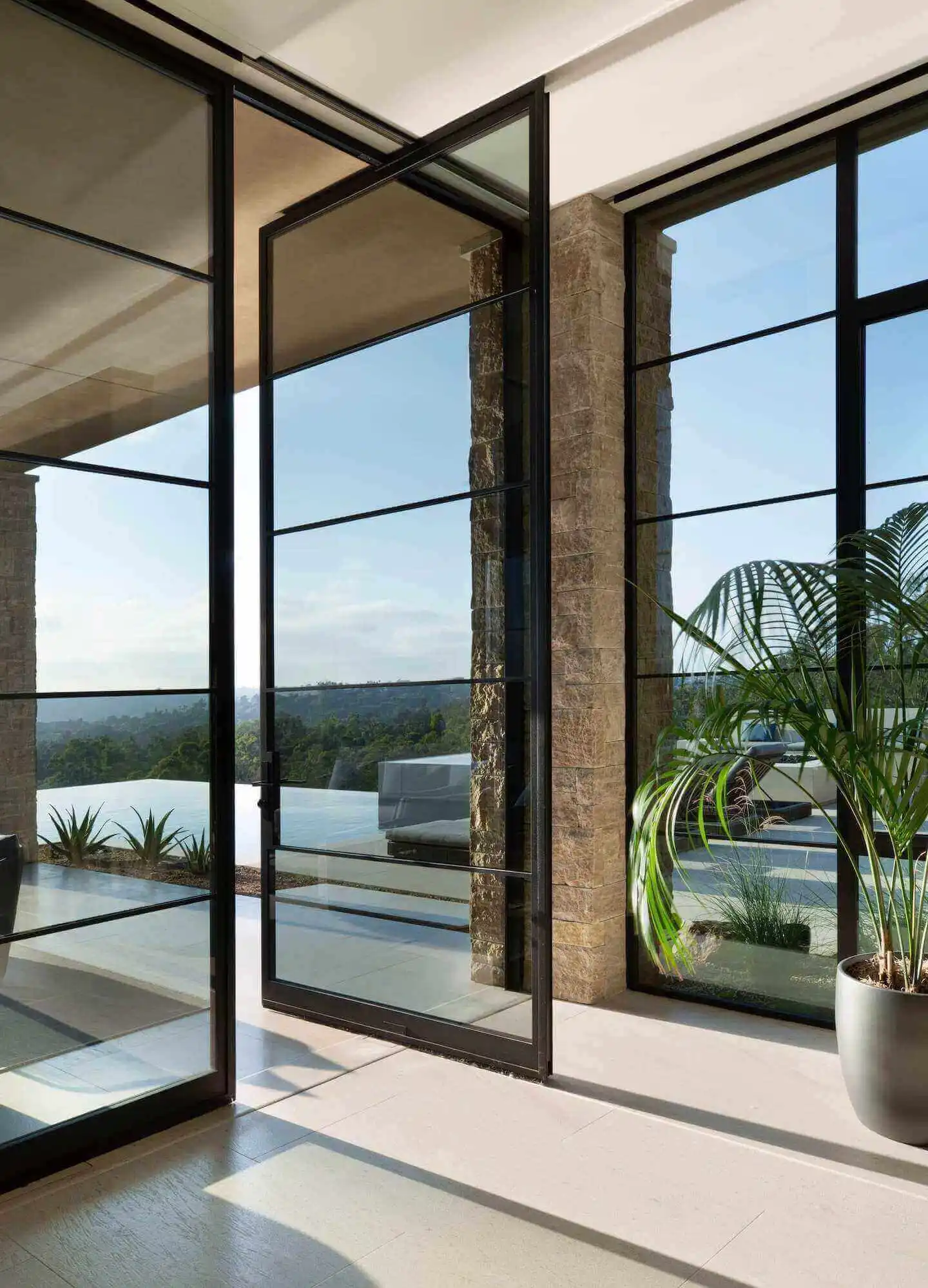 A large pivot glass door opens to reveal a room with a car parked just outside the entrance