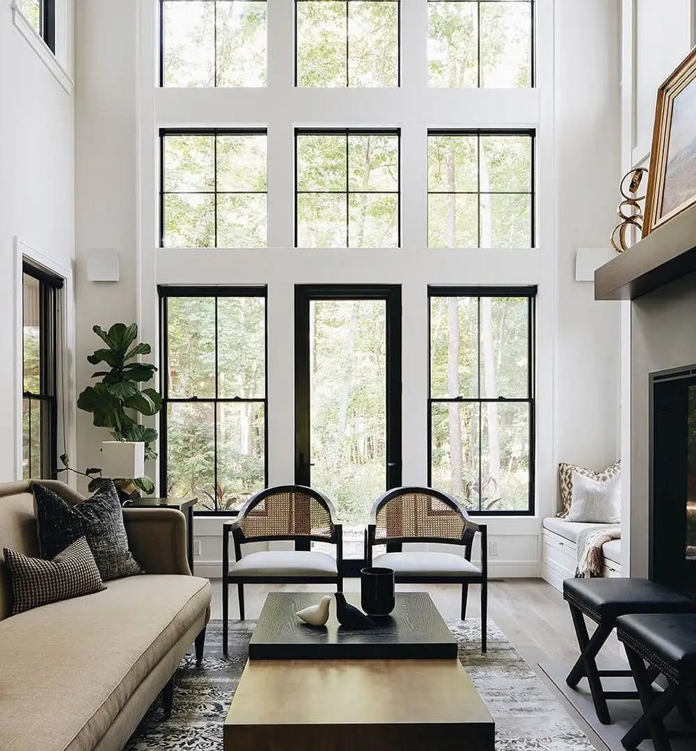 A modern living room featuring black and white furniture complemented by large windows along the wall for natural light