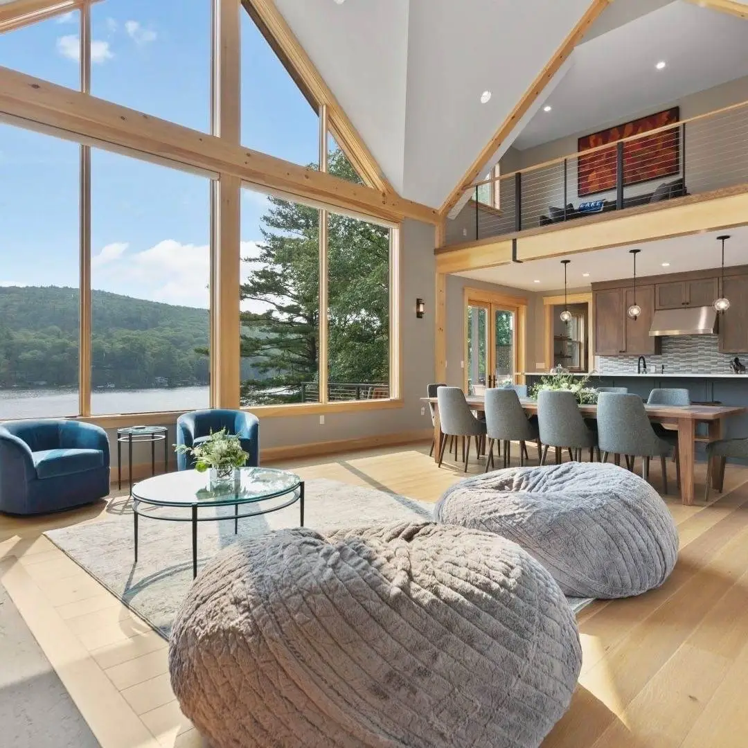 A spacious living room featuring a large window wall that offers a stunning view of the serene lake outside