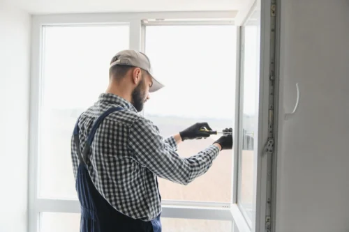 A man in overalls repairs a window securing it with nails for stability and safety