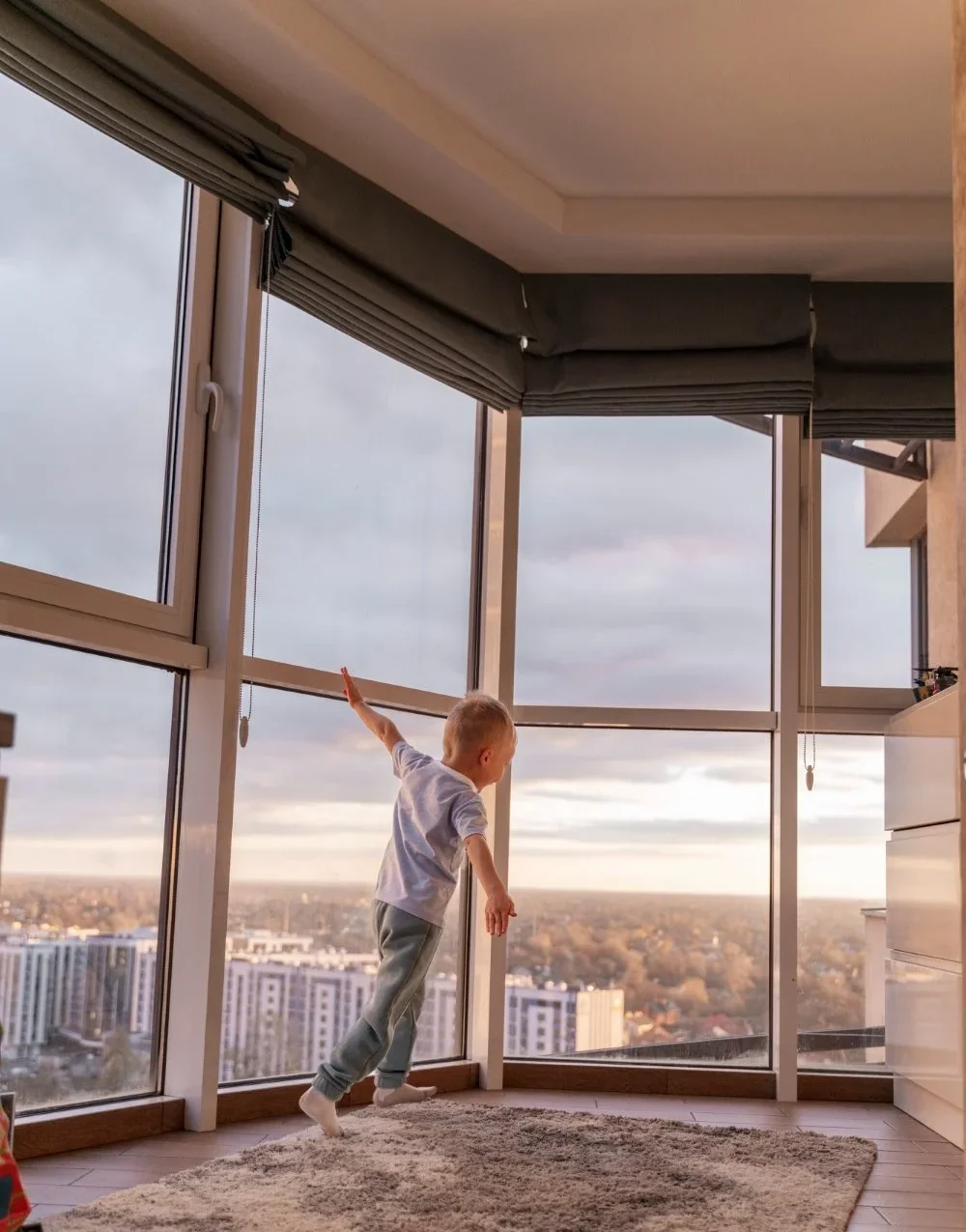 A child joyfully jumps in front of a large window capturing a moment of playfulness and energy indoors