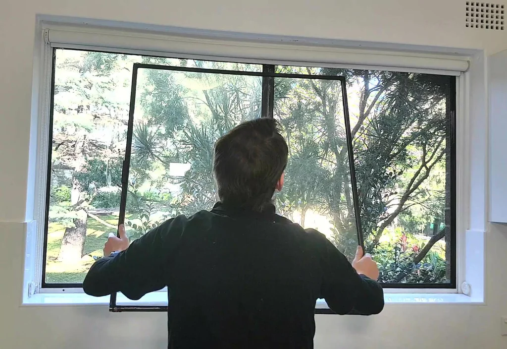 Man installing a black aluminum window screen from the inside