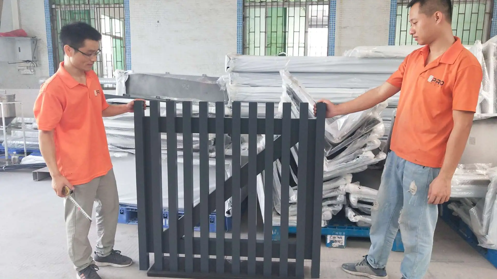 Two workers inspecting a metal fence panel in a factory