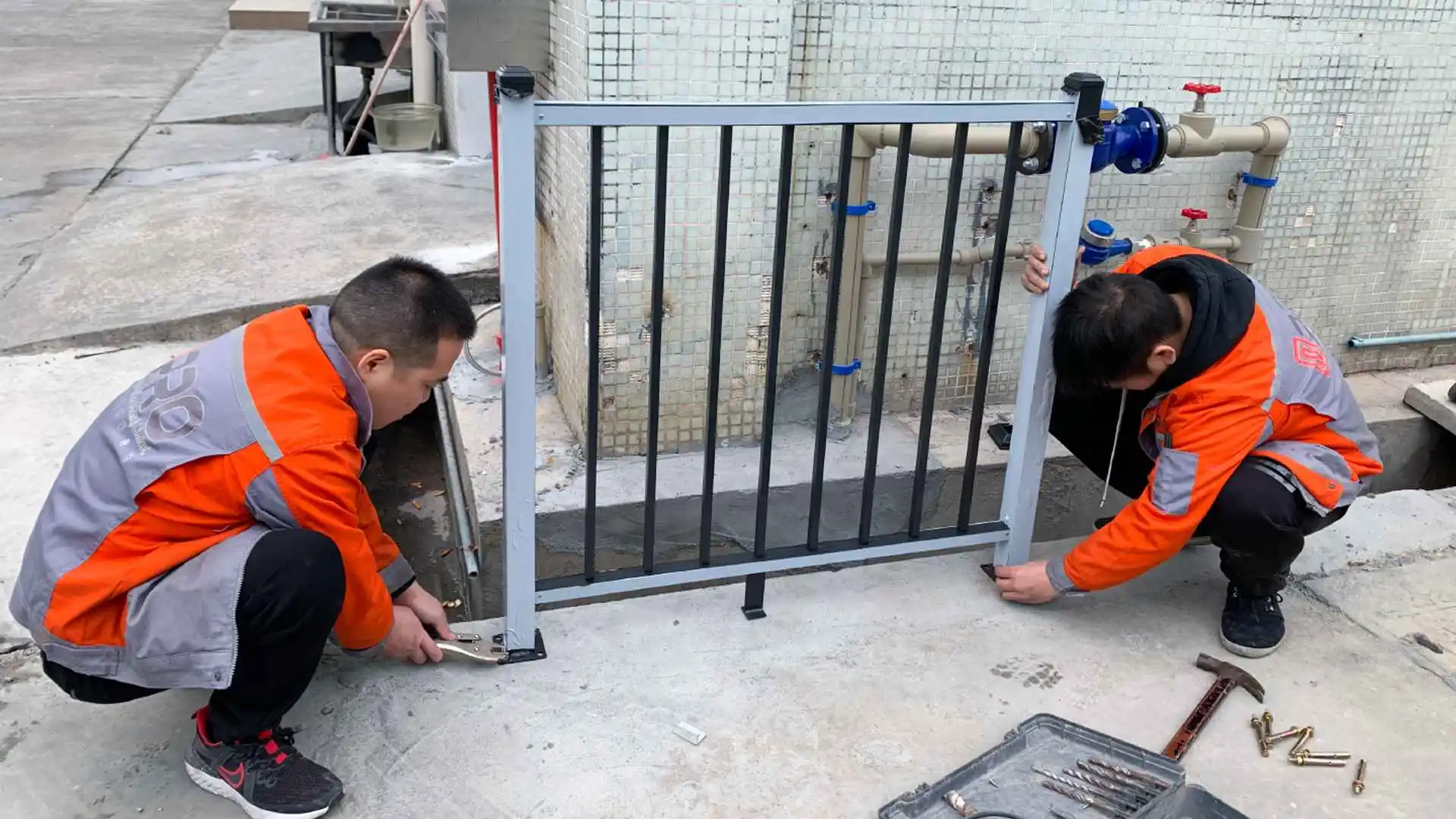 Two workers installing a small metal fence outdoors