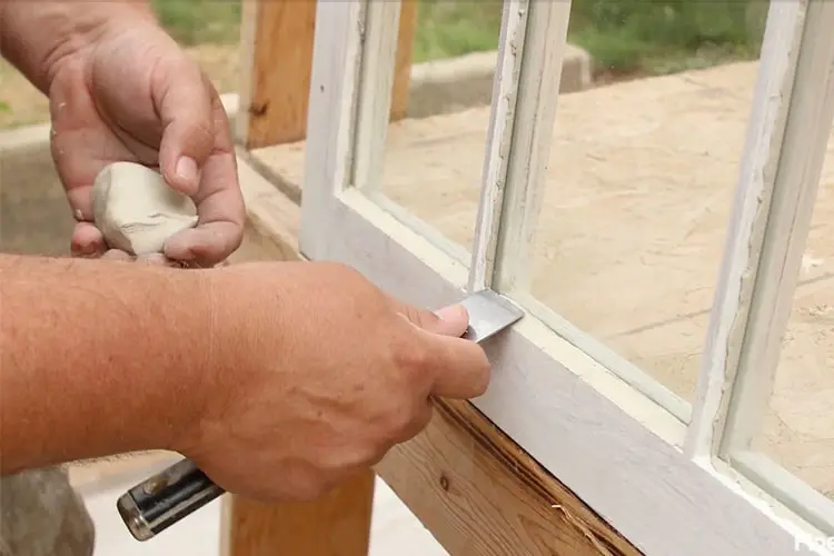 Worker applying putty to repair aluminum window frame close up