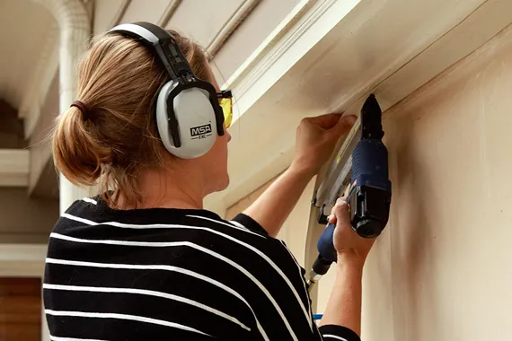 Worker with protective gear using nail gun for window frame repair