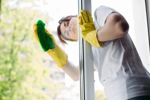 Uma pessoa limpando uma porta de vidro com luvas enfatizando a manutenção