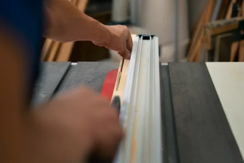 Worker guiding wood through table saw in workshop