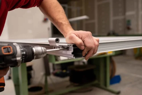 Worker securing hardware components to aluminum frames for window assembly