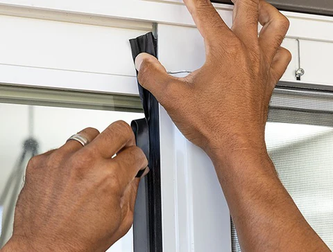 Close up of hands applying black weatherstripping on a door