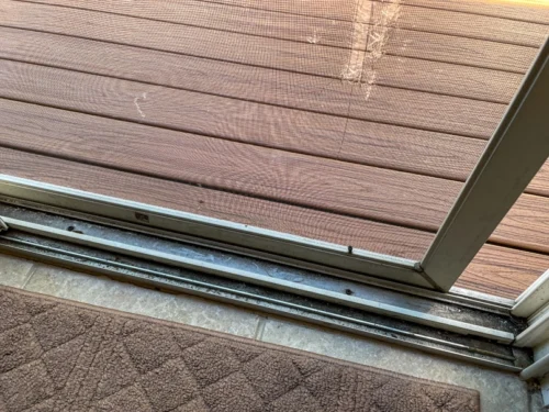 Glasschiebetürrahmen und Maschenschiene neben einem Holzdeck