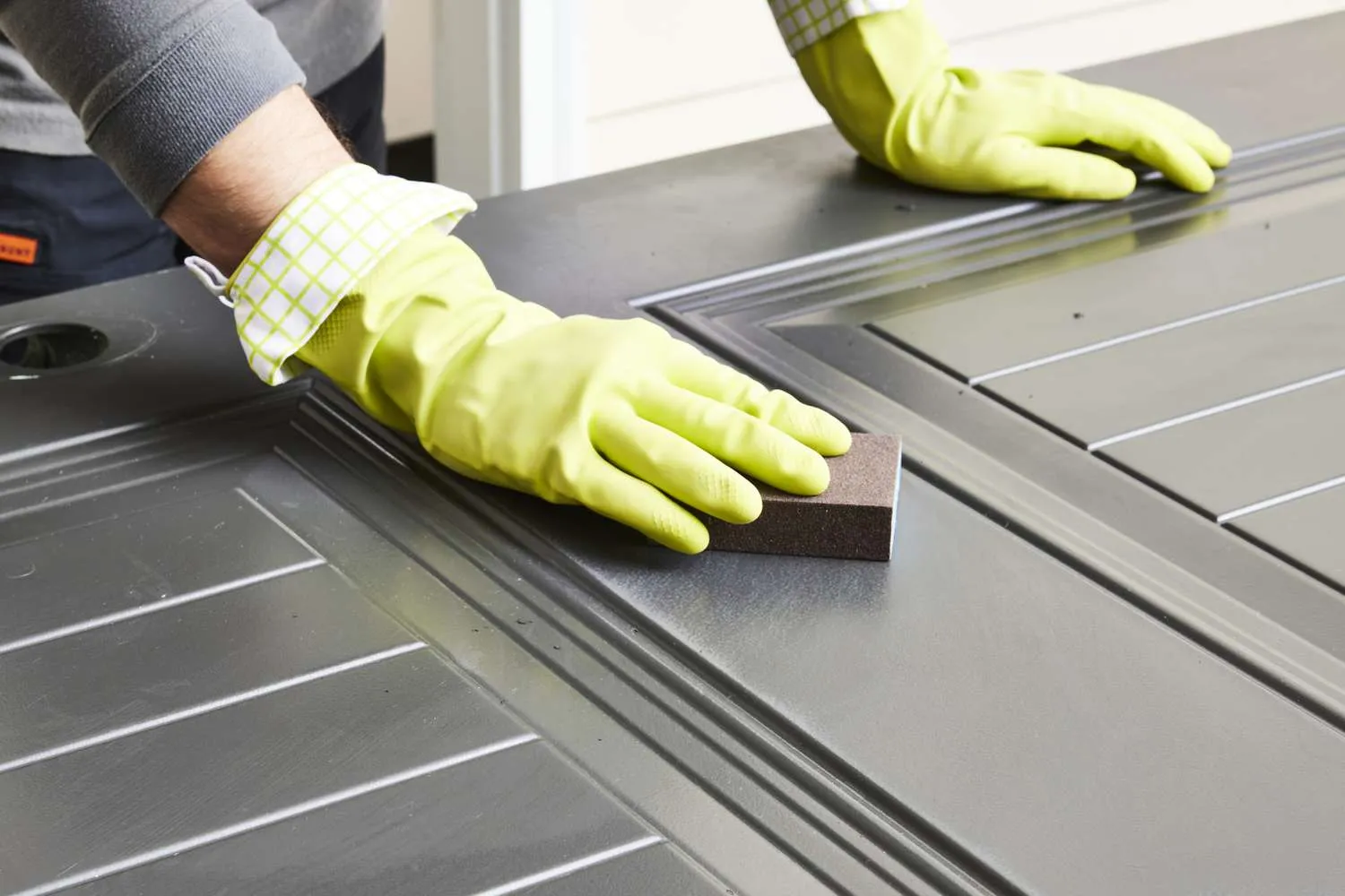 Person in gloves sanding aluminum door to prep for painting