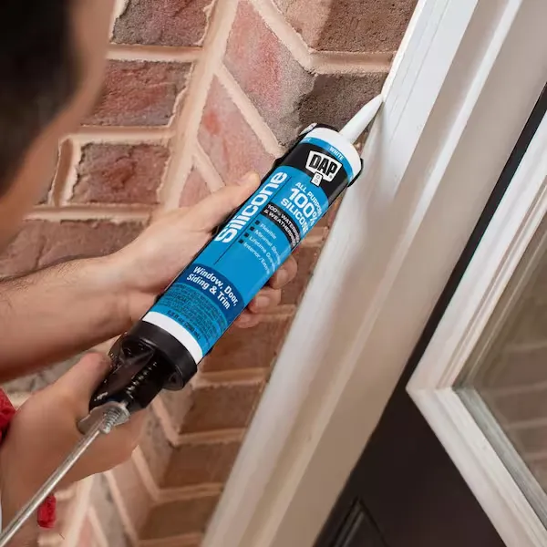 Person sealing door frame with clear silicone using caulk gun
