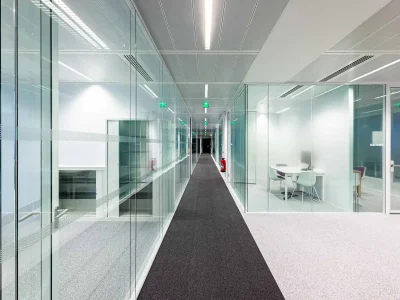 A spacious hallway with frameless glass partitions and a soft carpeted floor enhancing the sense of light and openness